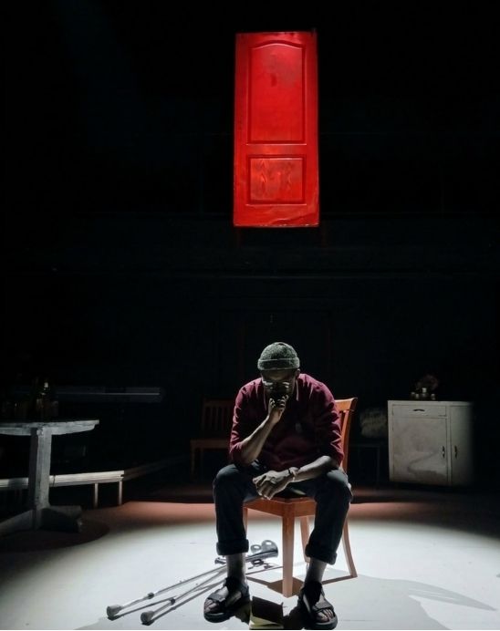 Mak Manaka seated on stage beneath a suspended red door
